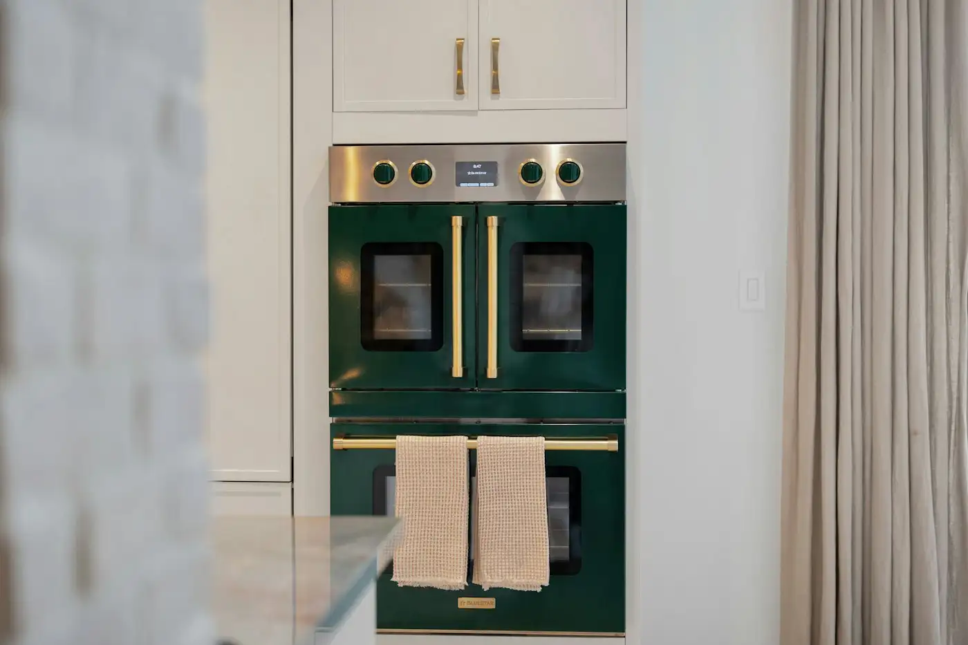 Stylish dark green double oven with brass handles and towels