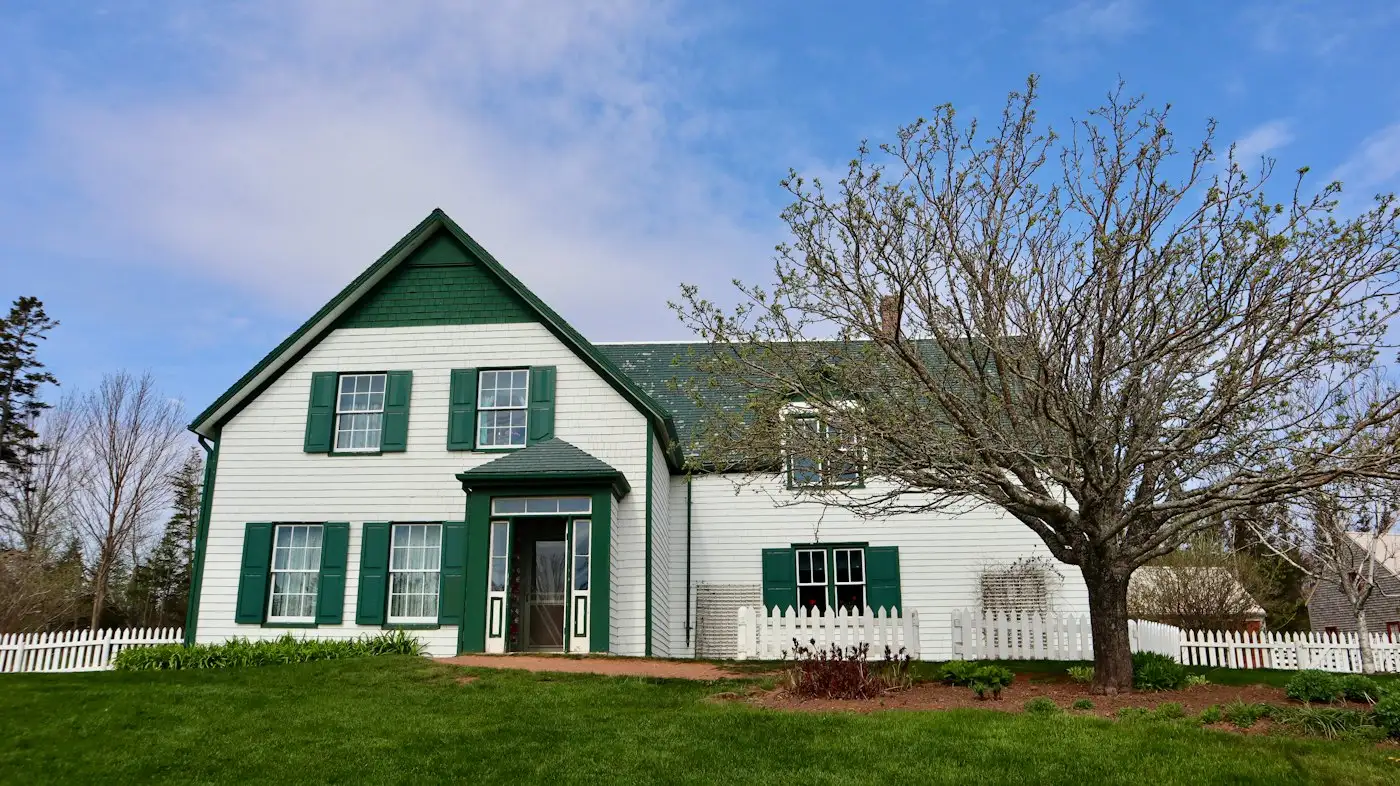 A white house with green shutters and a tree